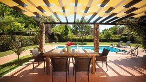 Une terrasse extérieure avec une piscine, une pergola offrant de l’ombre et une table avec des chaises.