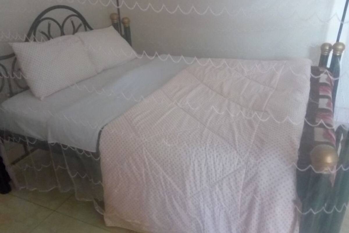 A bed with a metal frame, white bedding, and a sheer curtain.