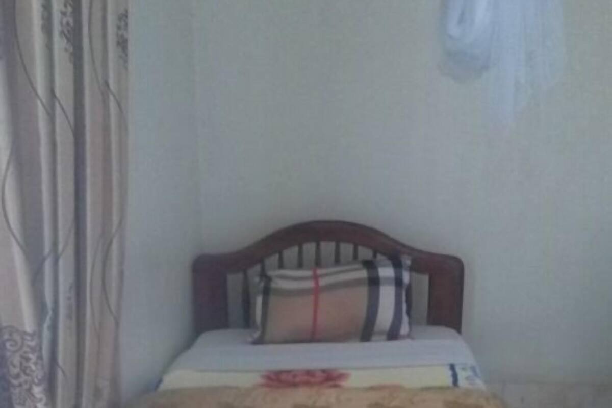 A bed with a wooden headboard, a patterned bedspread, and a white curtain on the left.