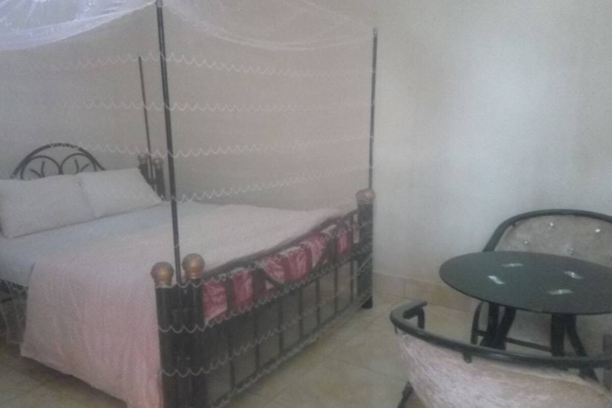 A four-poster bed with a canopy, a round table, and a chair in a room with plain walls.