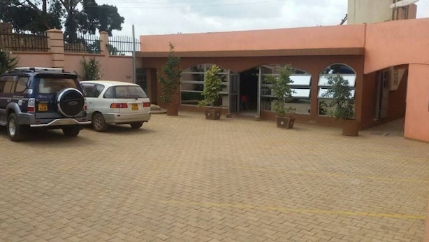 A building with a paved entrance area, two parked cars, and potted plants. - Kabz Hotel (Kampala)