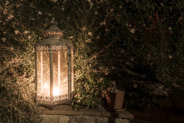 A lantern with intricate metalwork, placed on a stone ledge surrounded by dense foliage. - Romantic farm in the Sienese hills (Trequanda, Siena)