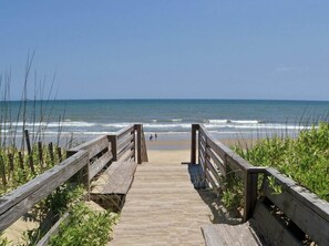 A wooden boardwalk leading to a beach with waves in the background.