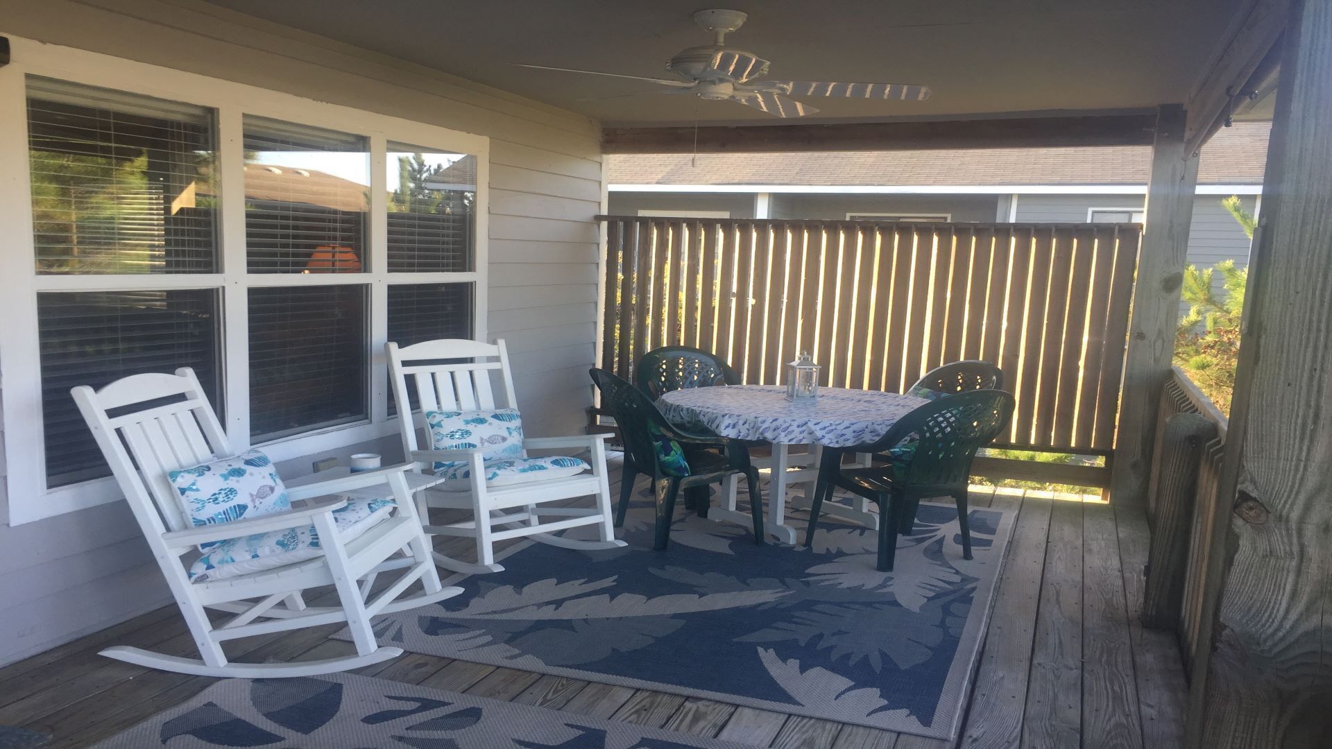 Een overdekt terras met een tafel, stoelen, een schommelstoel en een kamerkleed met een patroon.
