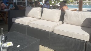 An outdoor seating area with a sofa and a table, overlooking a pool and palm trees. - Magnificent Beach front condo with pool and restaurant/bar (Freeport)