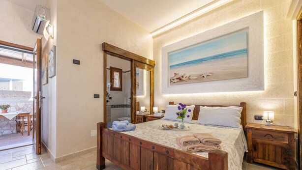 Une chambre à coucher avec un lit en bois, un tableau représentant la mer et une salle de bain visible à travers un miroir.