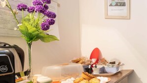 Une chambre d’hôtel avec un comptoir en bois, une machine à café, un vase avec des fleurs violettes, un panneau encadré indiquant que le Wi-Fi est gratuit, et un égouttoir à vaisselle contenant de la vaisselle.