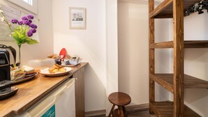 Une cuisine avec un plan de travail en bois, une machine à café, un vase rempli de fleurs violettes et un panneau encadré accroché au mur.