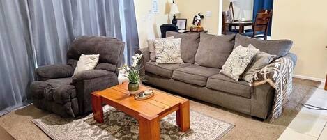 A living room with a sofa, armchair, wooden coffee table, and a patterned rug.