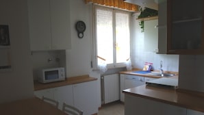 Ett kök med vita skåp, en mikrovågsugn, ett handfat och ett fönster med gardiner.