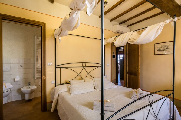 A bedroom with a four-poster bed, a bedside table, and a window.
