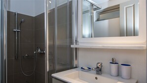Ein modernes Badezimmer mit einer gläsernen Duschkabine, einem weißen Waschbecken mit Spiegel darüber und zwei zylindrischen Behältern auf der Ablagefläche.