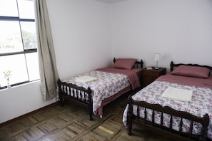 A room with two wooden beds, a window with curtains, a bedside table with a lamp, and a wooden floor. - Private room with independent entrance and private bathroom for 2 persons (Cercado de Lima)