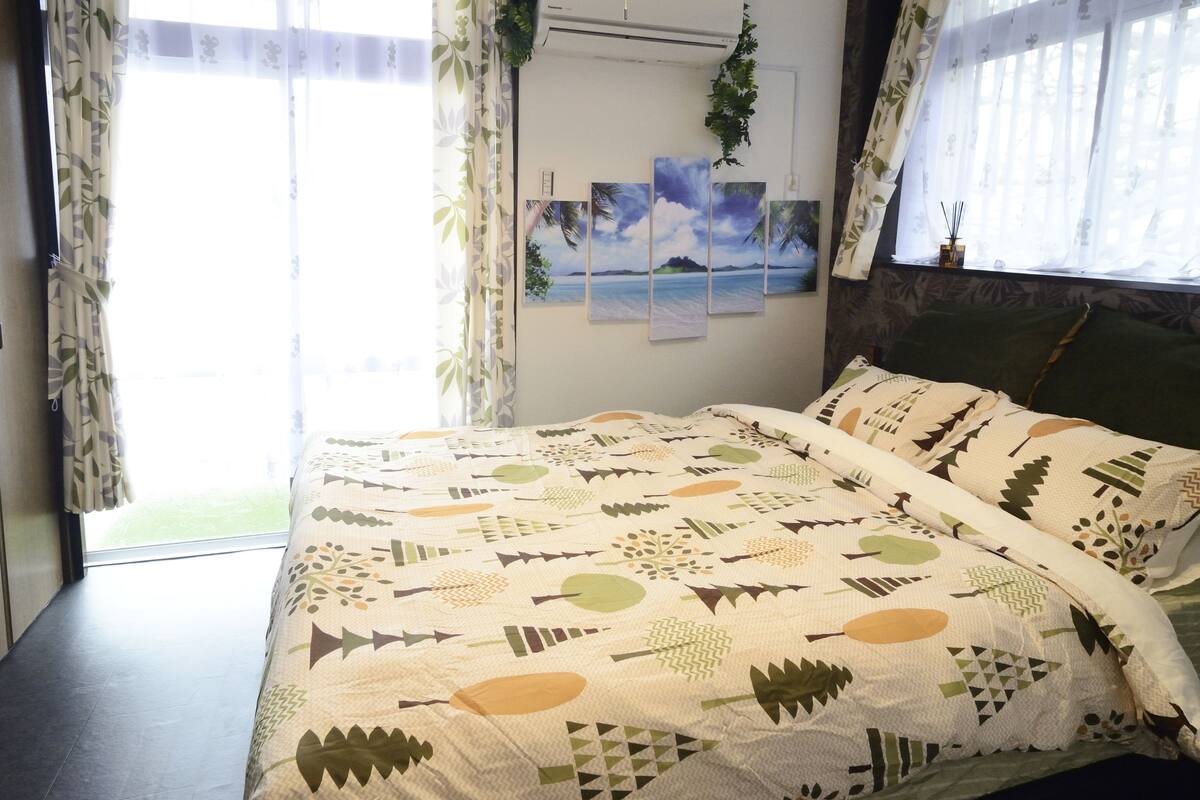 A bed with a patterned quilt, a window with curtains, and a wall with a painting.