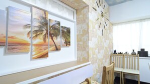 A room with a wall-mounted clock, a wooden chair, and three framed sunset paintings. - South Island (Itoman)