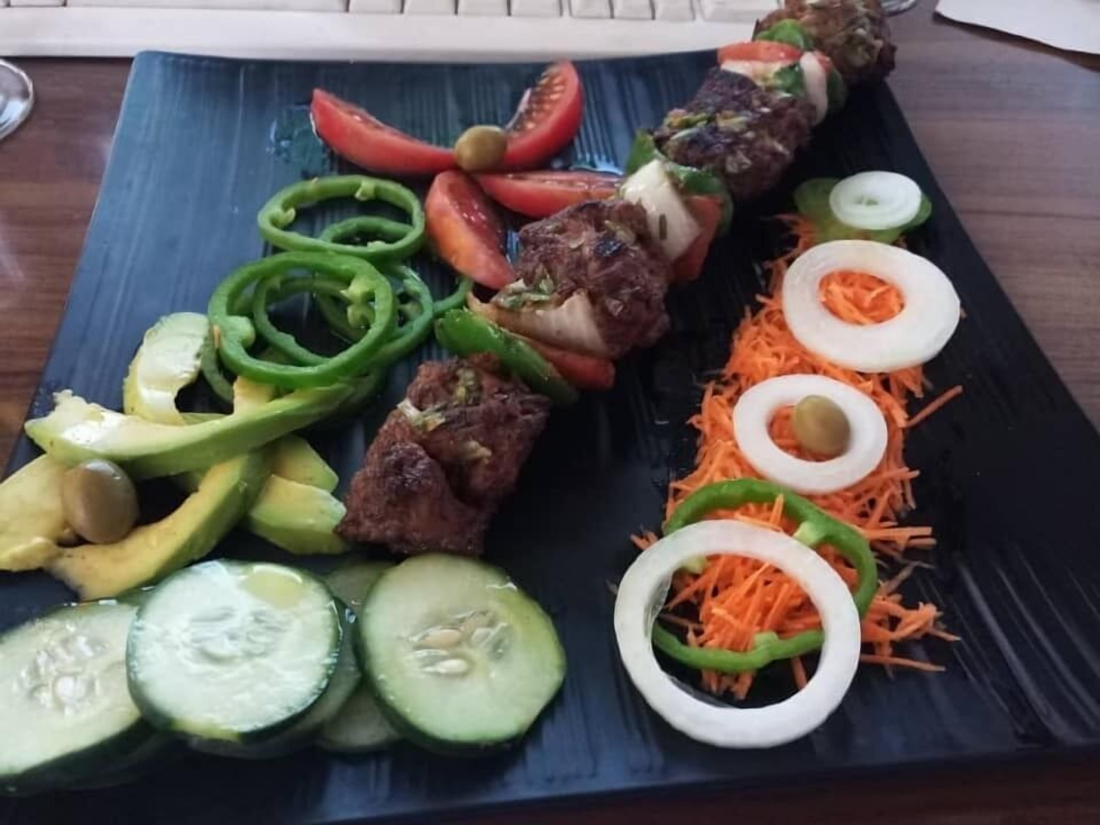 En tallrik med olika sorters mat, inklusive köttspett, grönsaker och garnering.