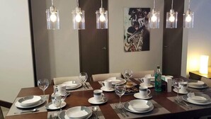Un espace repas avec une longue table dressée pour le repas, plusieurs luminaires et une œuvre d’art murale.