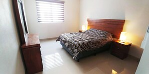 Een slaapkamer met een bed, twee nachtkastjes, een raam met zonwering en een spiegel.