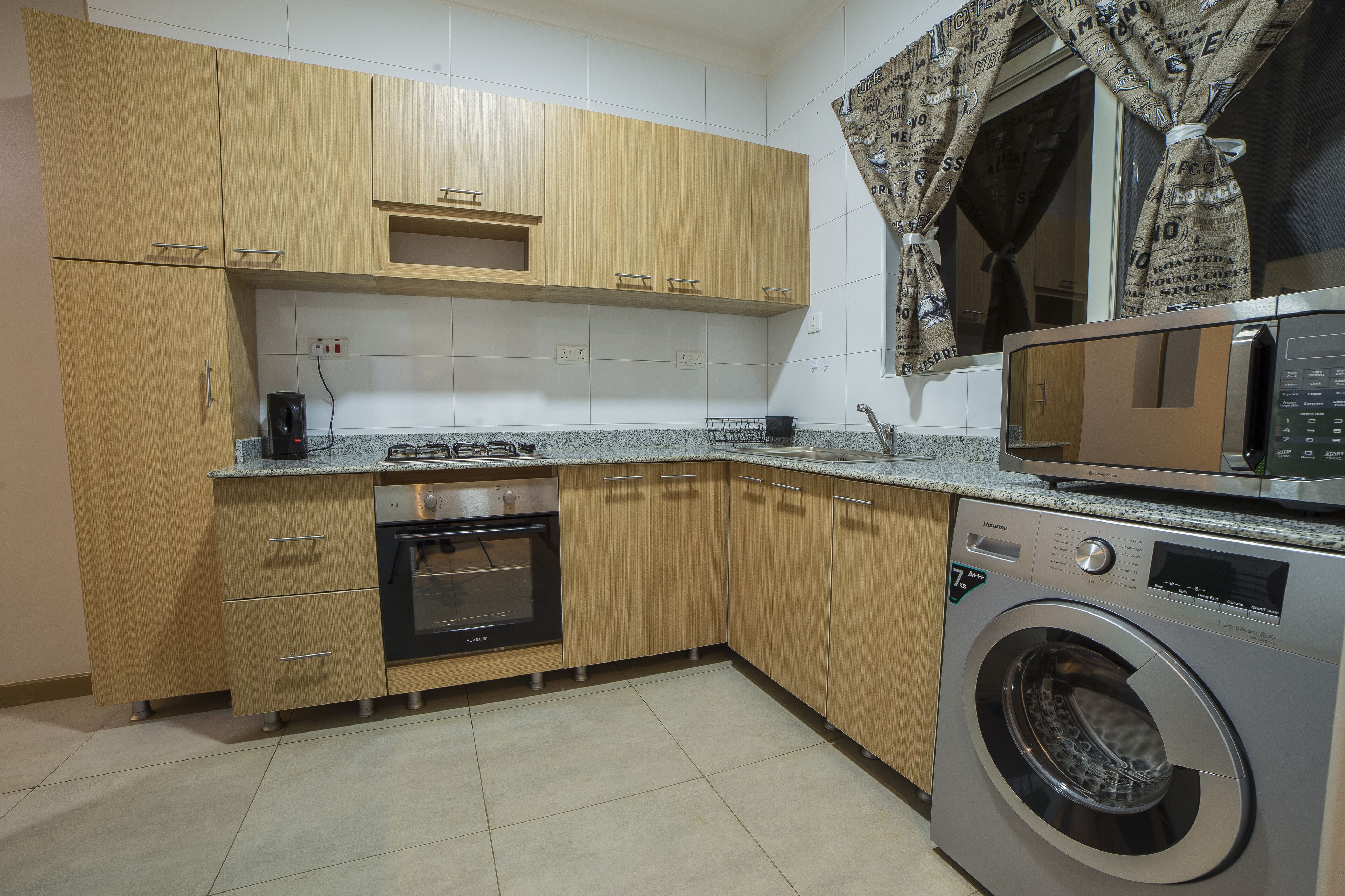 A kitchen with wooden cabinets, a built-in oven, a washing machine, and a microwave.