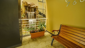 A reception area with a wooden bench, a potted plant, a small waterfall feature, and a wall with numbers. - Natra Apartments (Kampala)