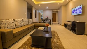 A modern living room with a sectional sofa, a coffee table, and a flat-screen TV mounted on the wall. - Natra Apartments (Kampala)