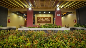 A building entrance with a sign reading "Natra Apartments," surrounded by greenery and benches. - Natra Apartments (Kampala)