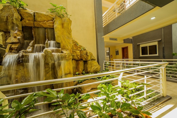 A hotel lobby with a waterfall feature, a railing, and potted plants.