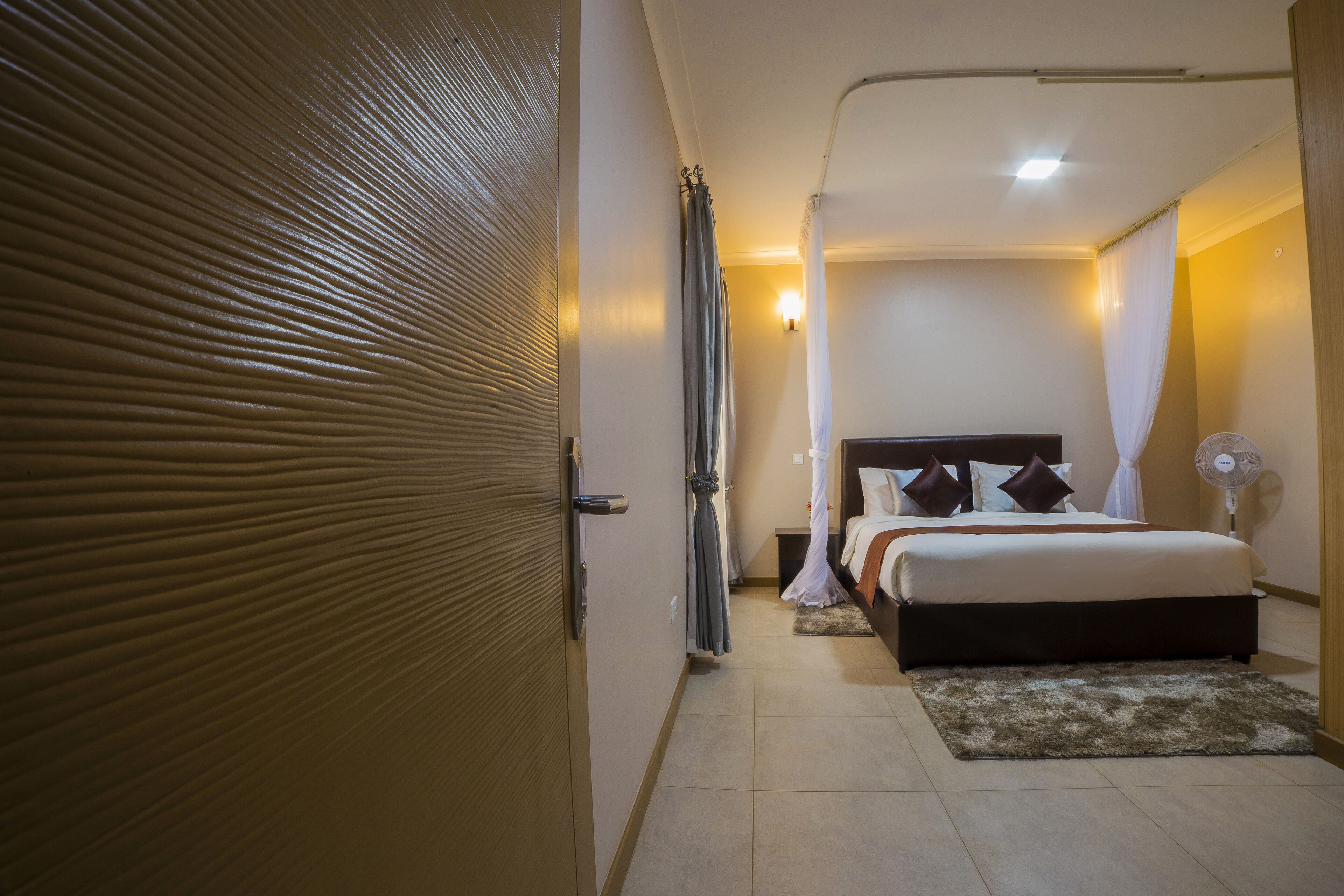 Un dormitorio con cama, mesita de noche, cortinas y ventilador de techo.