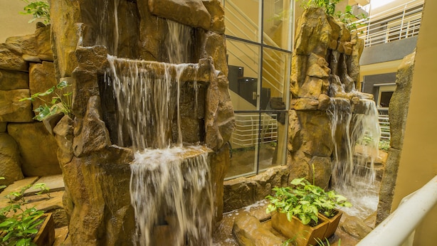 A multi-level indoor waterfall feature with cascading water, surrounded by rock formations and potted plants. - Natra Apartments (Kampala)