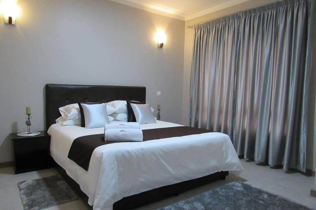 A hotel room with a large bed, two bedside tables, a nightstand, a rug, and a curtain.