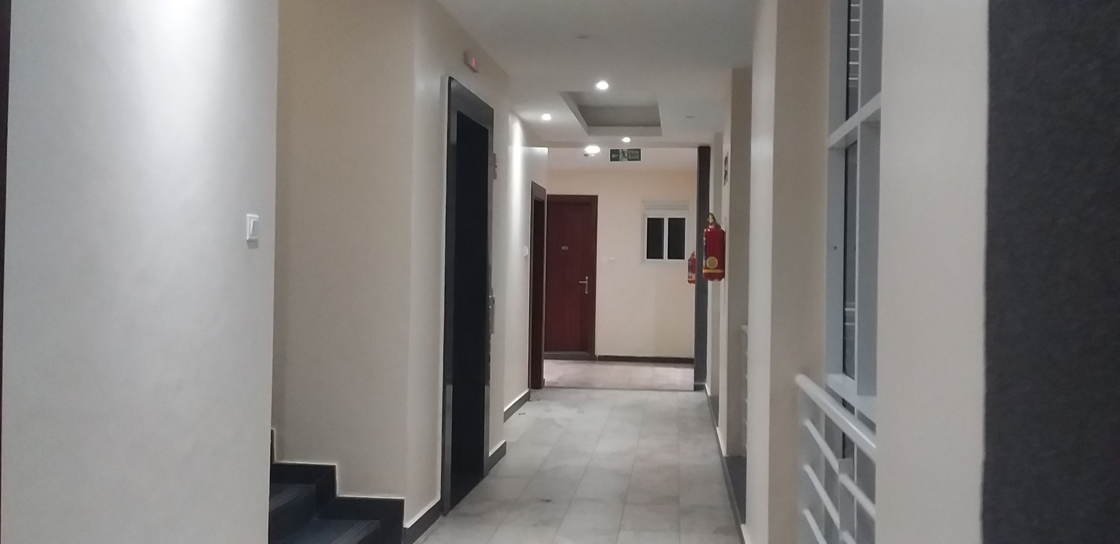 A corridor with a fire extinguisher mounted on the wall, a door at the end, and a staircase on the left.