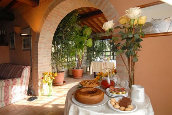 A cozy dining area with a brick archway, a table set with a cake, pastries, and a vase of flowers.