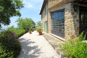 A stone building with a gravel path, potted plants, and a view of the sea.