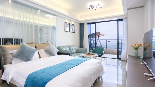 A modern hotel room with a large bed, a sofa, a TV, and a balcony with a view. - Seacliff Apartment (Shantou)