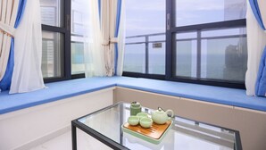 A room with a glass table, a window seat with blue cushions, and a view of the sea. - Seacliff Apartment (Shantou)