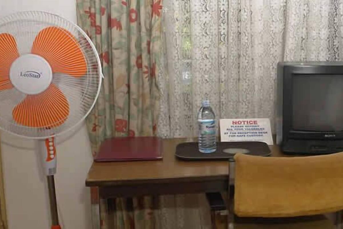 A room with a desk, a television, a fan, a chair, and a lamp.
