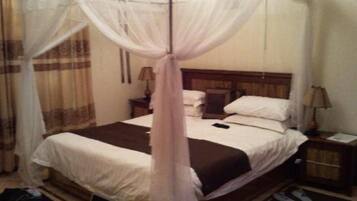 A bed with a canopy, a bedside table, a lamp, and a pair of slippers on the floor.