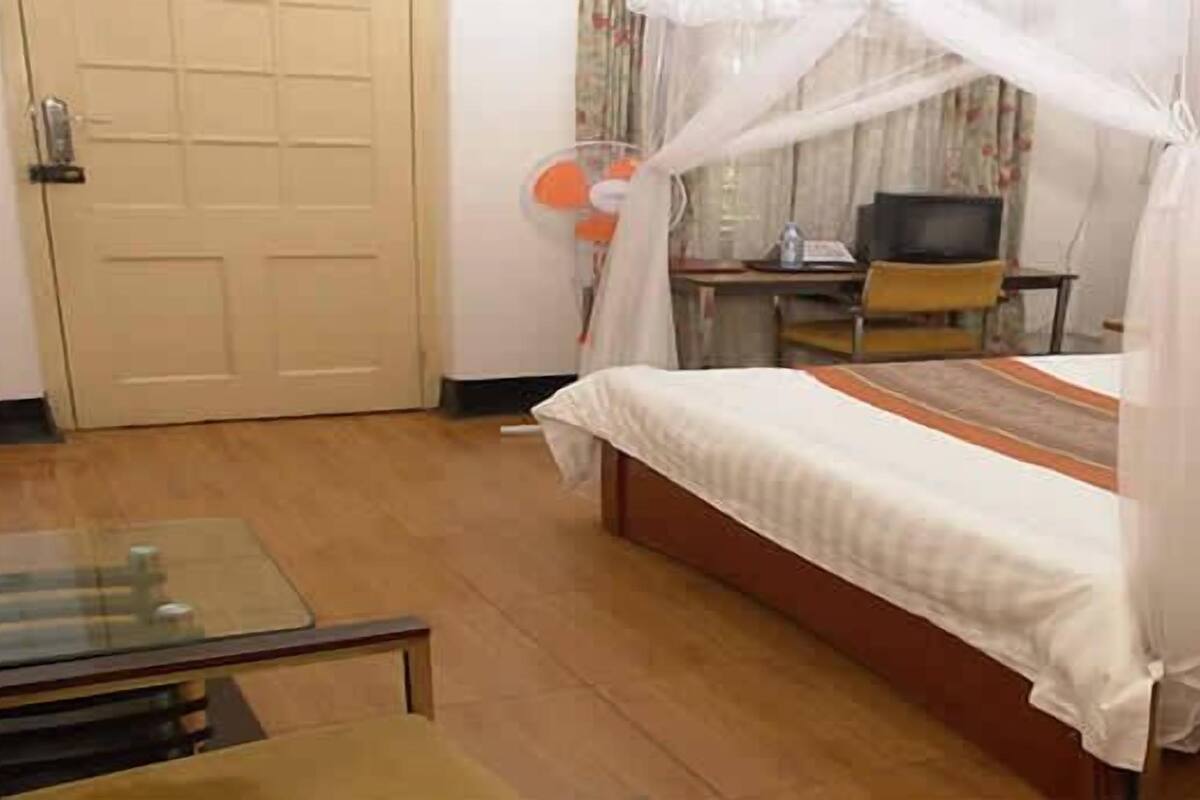 A bedroom with a bed, a bedside table, a chair, a desk with a computer, and a television.
