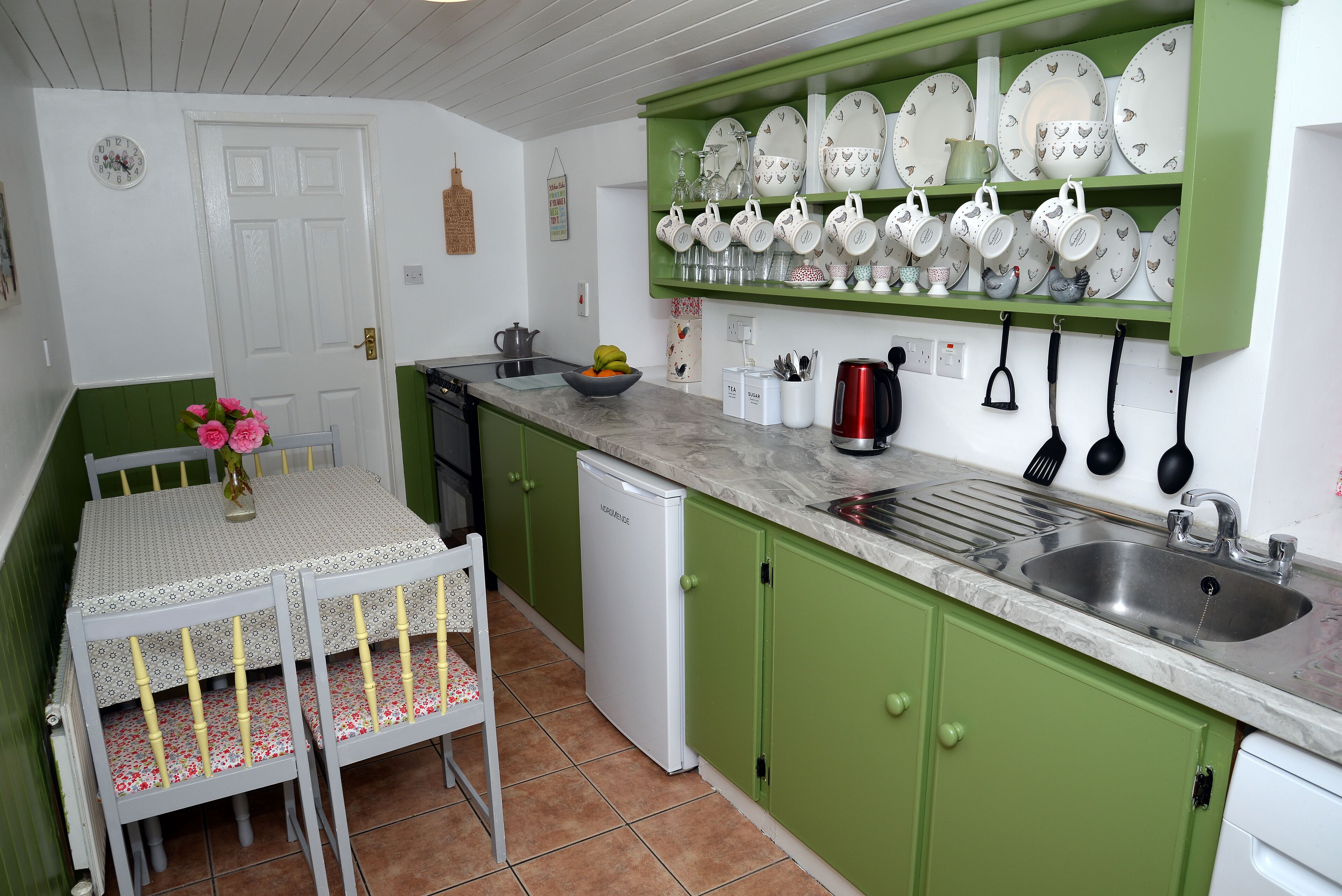 A kitchen with green cabinets, a white refrigerator, a sink, and a dining table with chairs.