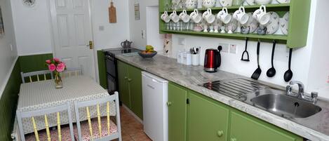 A kitchen with green cabinets, a white refrigerator, a sink, and a dining table with chairs.