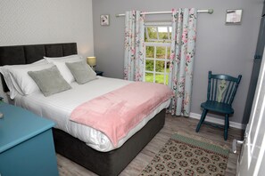 A bedroom with a bed, pillows, a bedside table, a chair, a window with curtains, and a door. - Cloverhill  Gate Lodge       Relax Refresh and Unwind  promises tranquillity (Co Cavan)