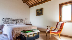 A bedroom with a bed, a nightstand, a chair, a suitcase, and a painting on the wall. - Marotta Chalet, on the slopes of Erice (Valderice)