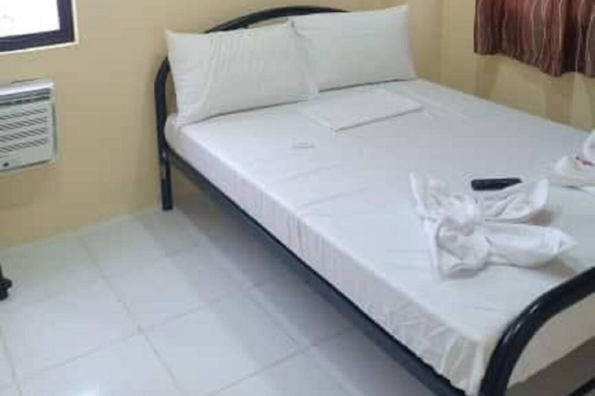 A single bed with white bedding, a window with blinds, a radiator, and a curtain on the wall.