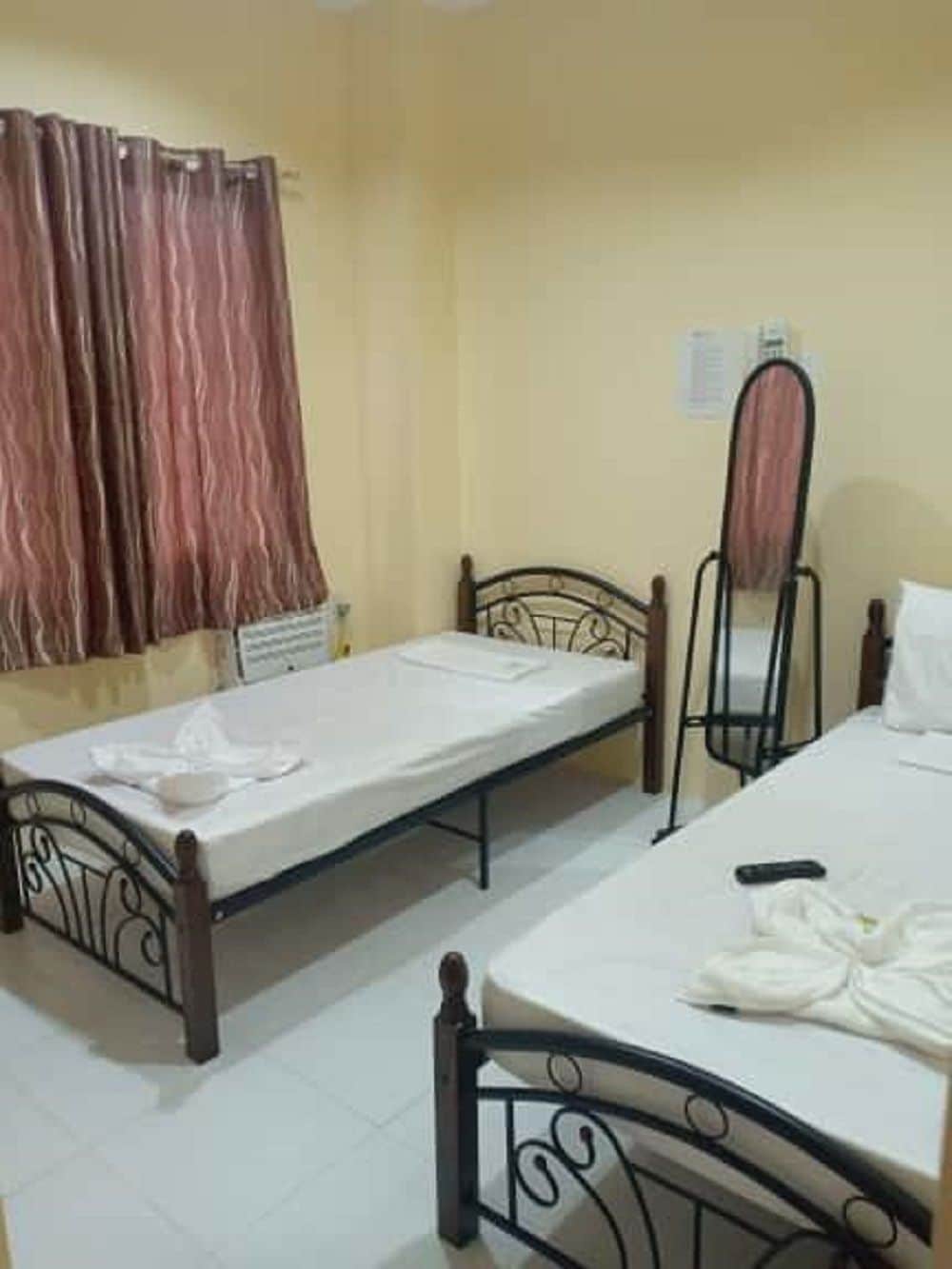 A small room with two single beds, a chair, a radiator, and a curtain.