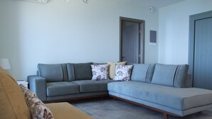 Ein Wohnzimmer mit einem grauen Ecksofa, einem beigen Sessel und gemusterten Kissen.