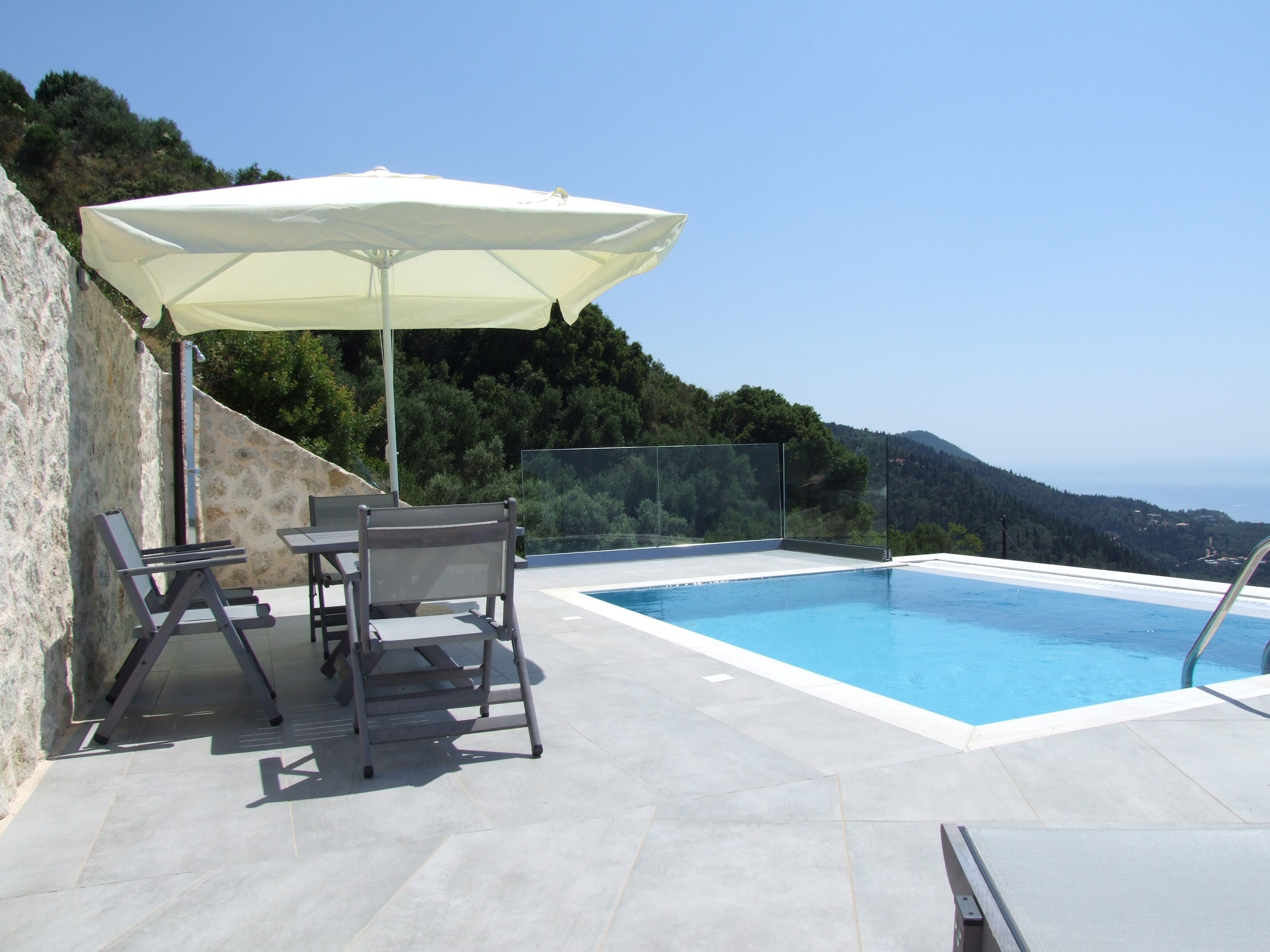 Ein Pool im Freien mit freiem Blick auf die umliegende Landschaft, ein Tisch mit Stühlen und ein weißer Sonnenschirm.