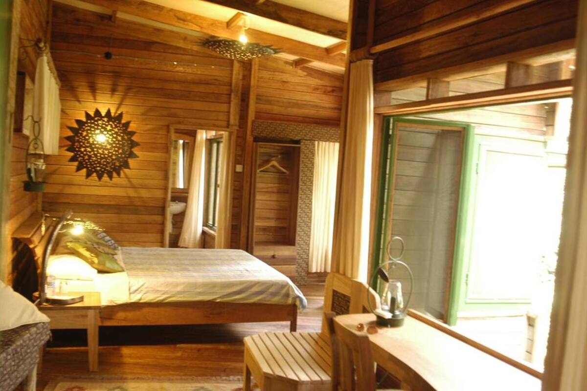 Quarto de cabana de madeira com uma cama, uma mesa e um candeeiro suspenso.