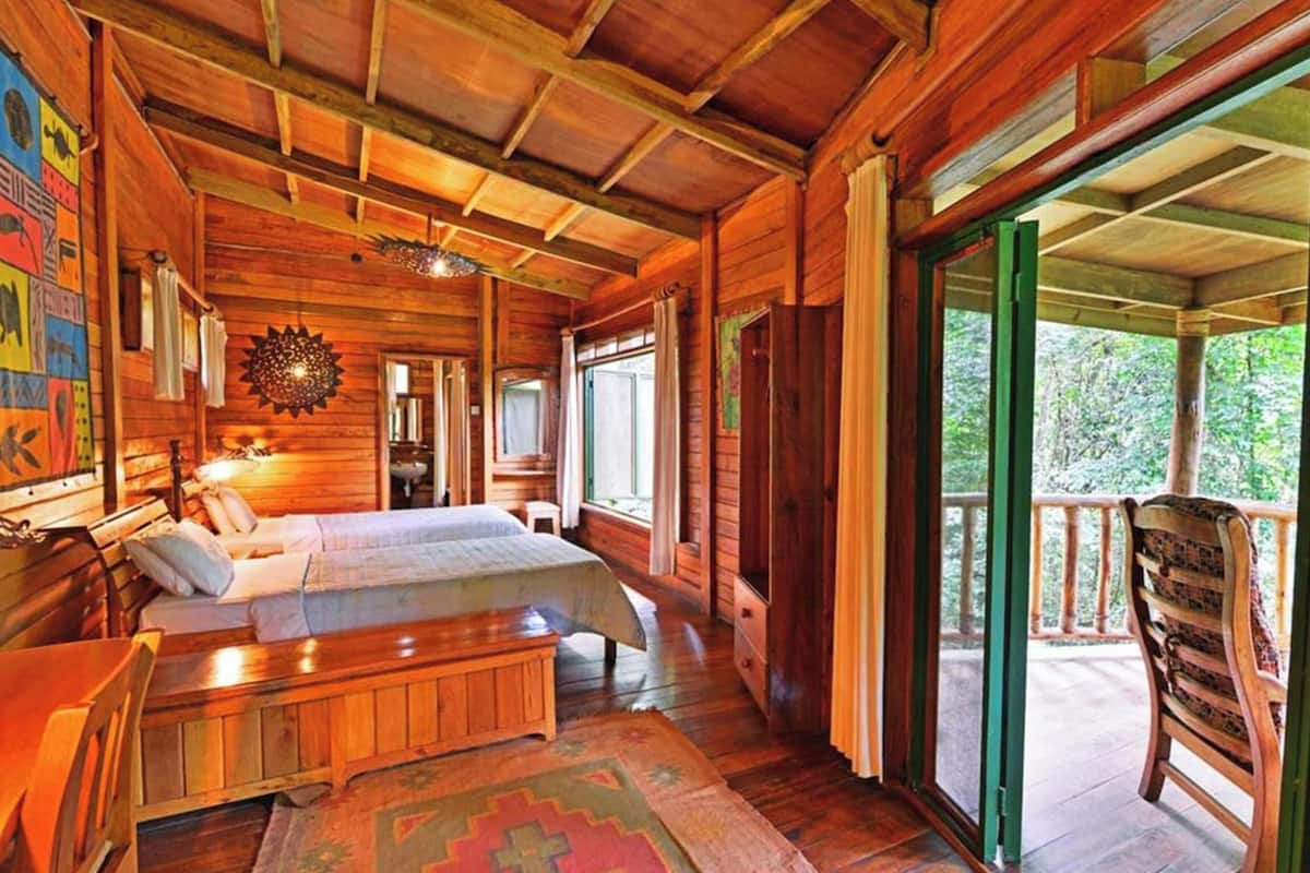Uma cabana de tronco com interior de madeira, uma cama, um banco e uma varanda com uma cadeira.