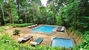 A pool area surrounded by lush greenery, with lounge chairs and a small hot tub. - The Rainforest Geo Lodge (Lugazi)