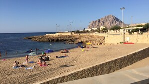 Een strand met mensen die zonnen en zwemmen, een rotsachtige kustlijn en een berg op de achtergrond.